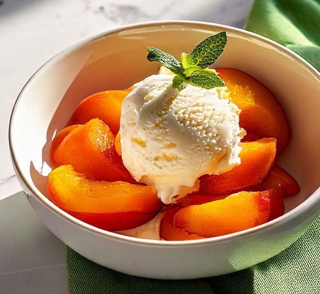 Bowl of caramelized peach topped with Breyers Vanilla ice cream.