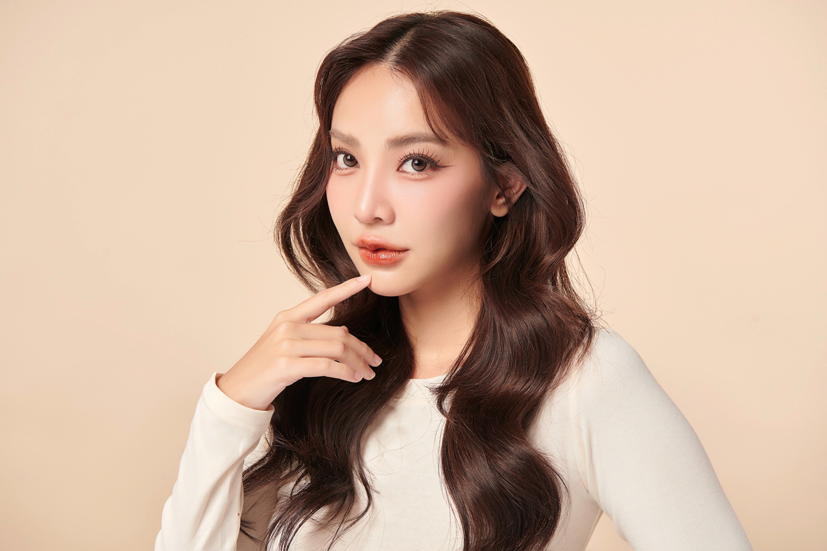 สาวเอเชีย ผิวขาวเหลือง ผมยาว แต่งหน้าโทนสีน้ำตาล มือแตะริมฝีปากล่าง