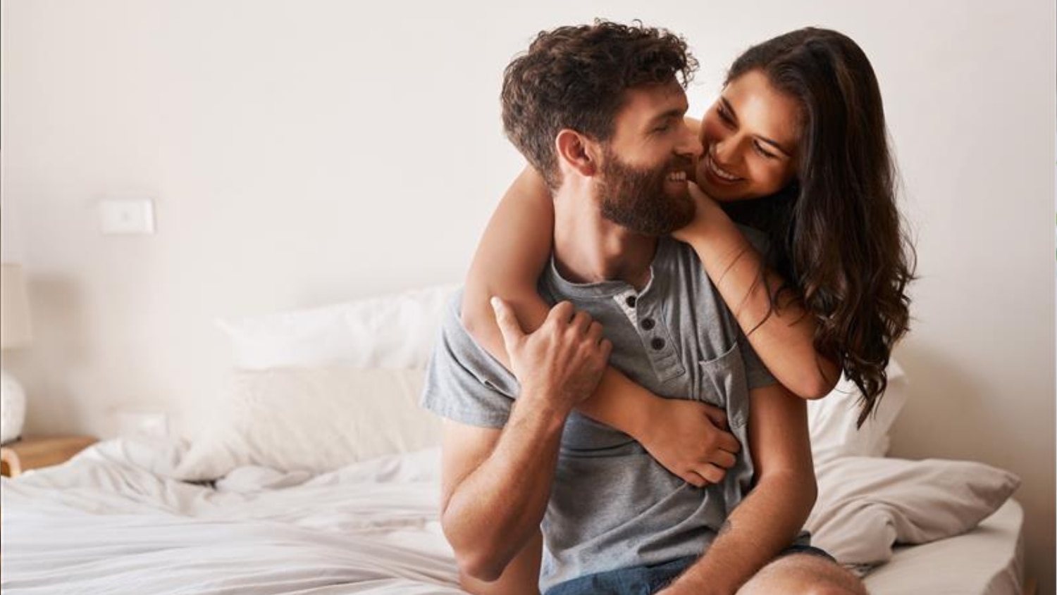 Happy couple cuddling on their bed while the man is wearing his signature scent