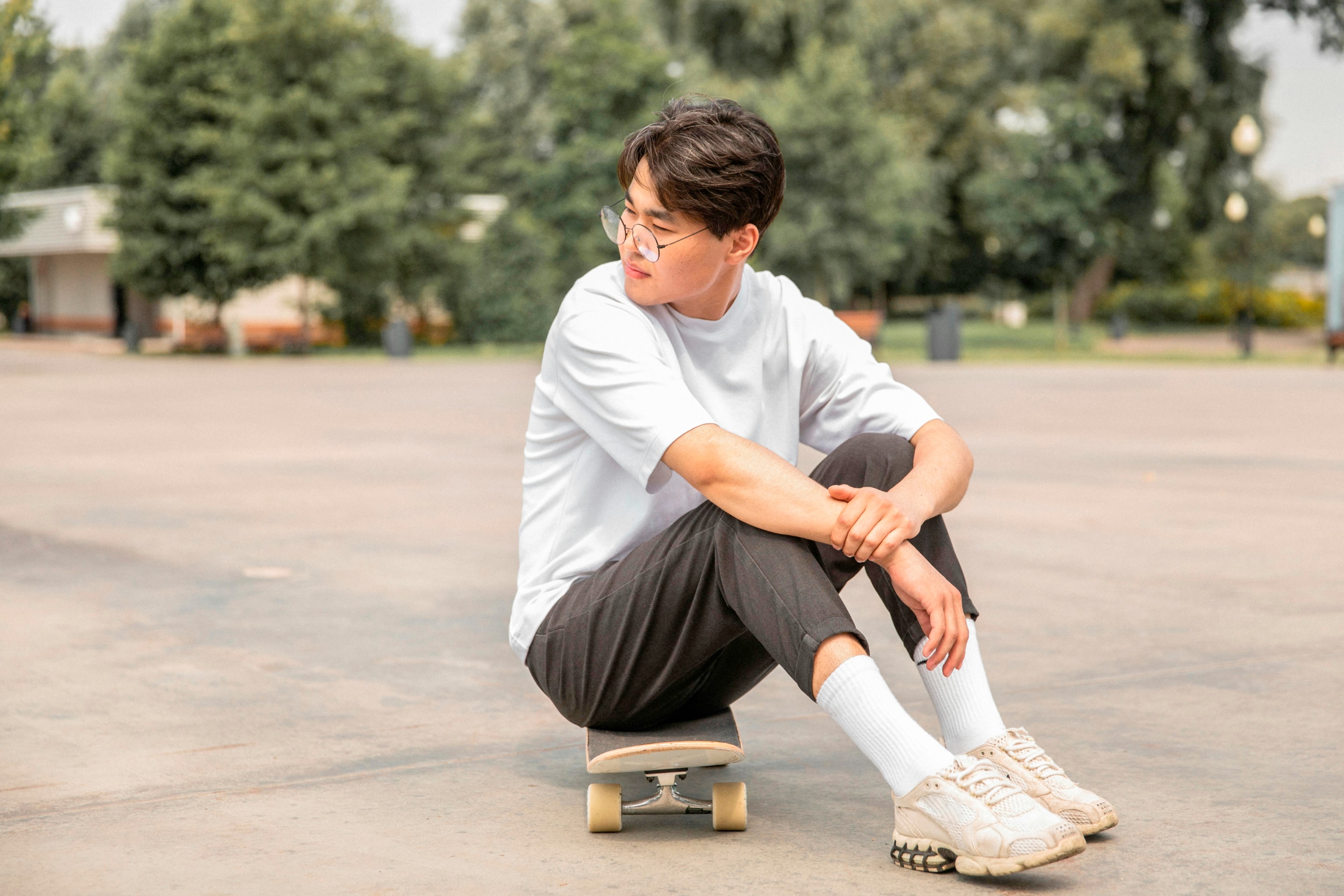 pria asia dengan gaya smart casual yang sedang duduk di atas skateboard