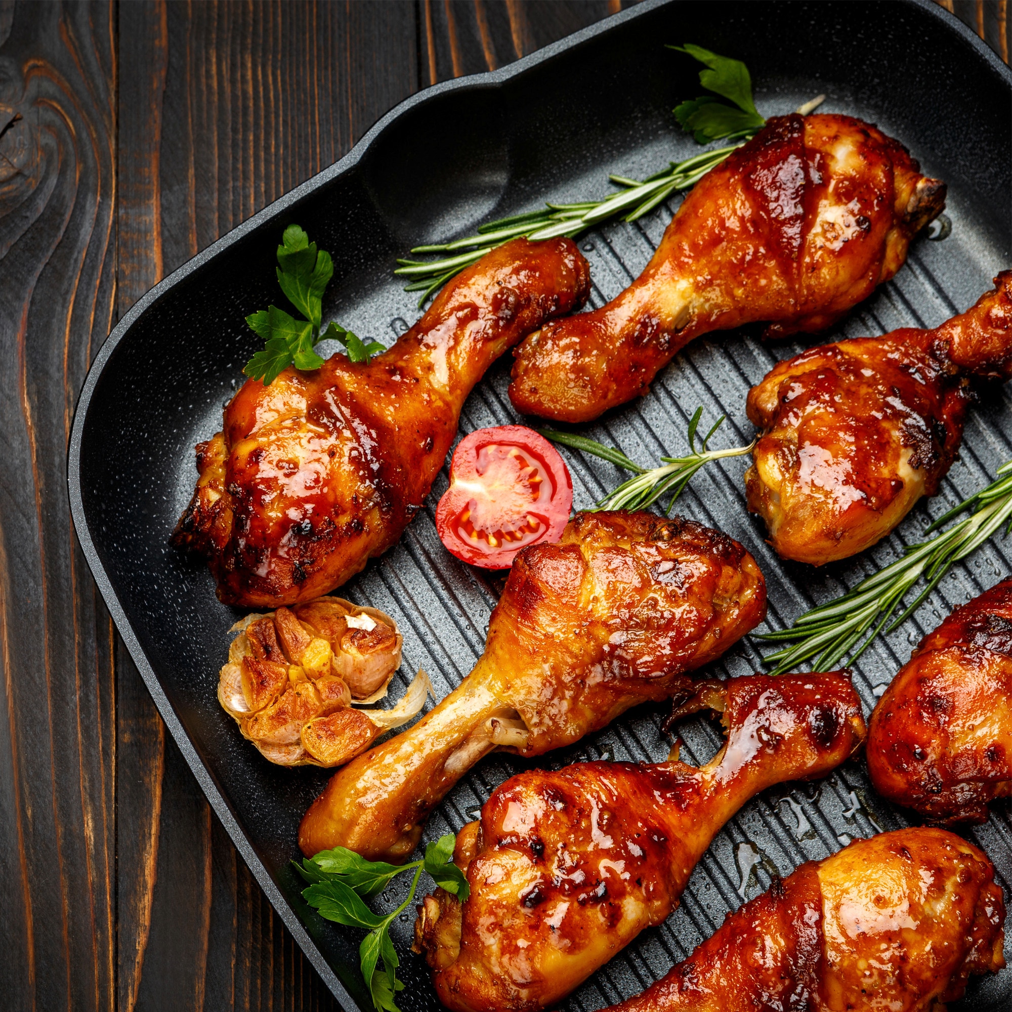 Whole roasted chicken in a roasting dish with potatoes,onions and tall sprig of rosemary with a bowl of pomagranate seeds on the side.
