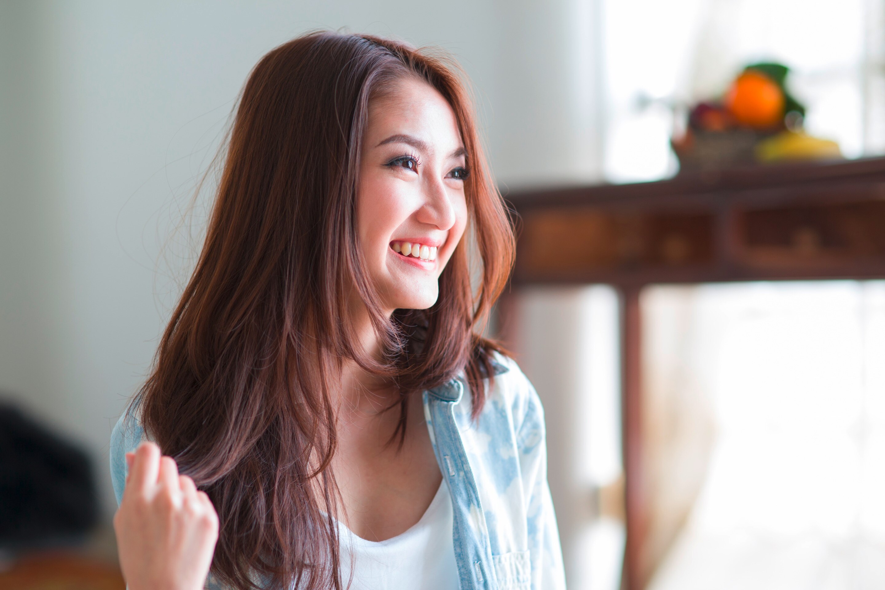 Woman with long hair and a smiling face sitting near a window.