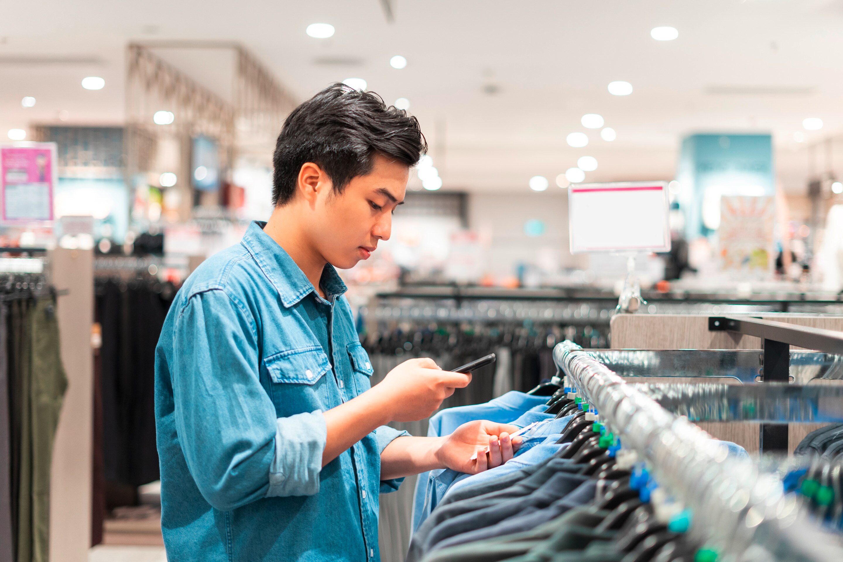 Man in denim shirt looking at tag while shopping.