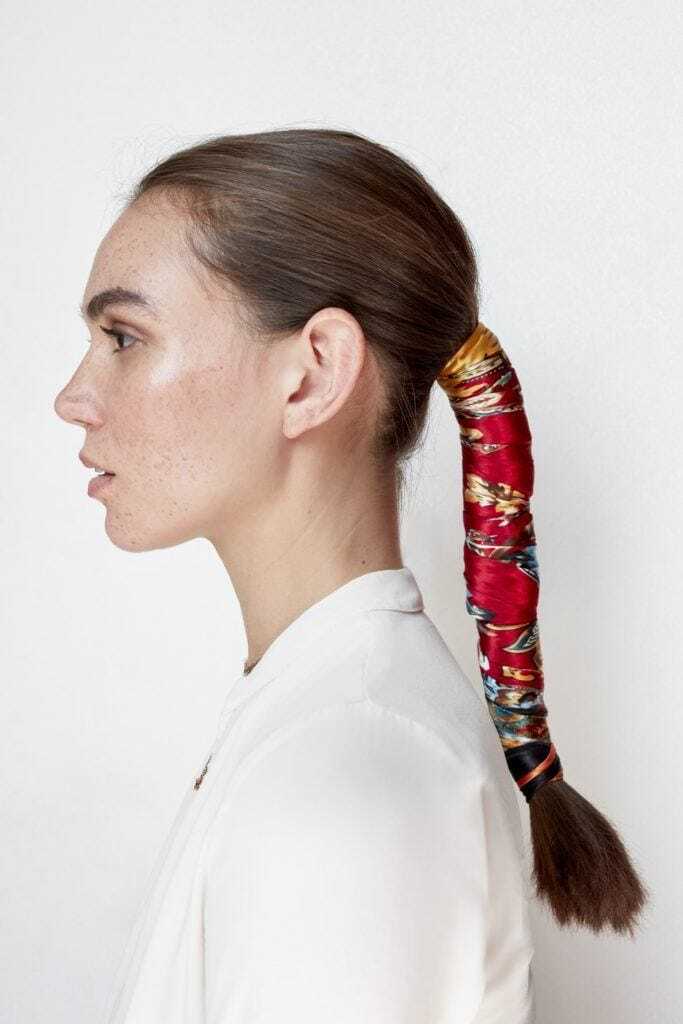 Woman with brown long hair in low ponytail wrapped with a red headscarf.