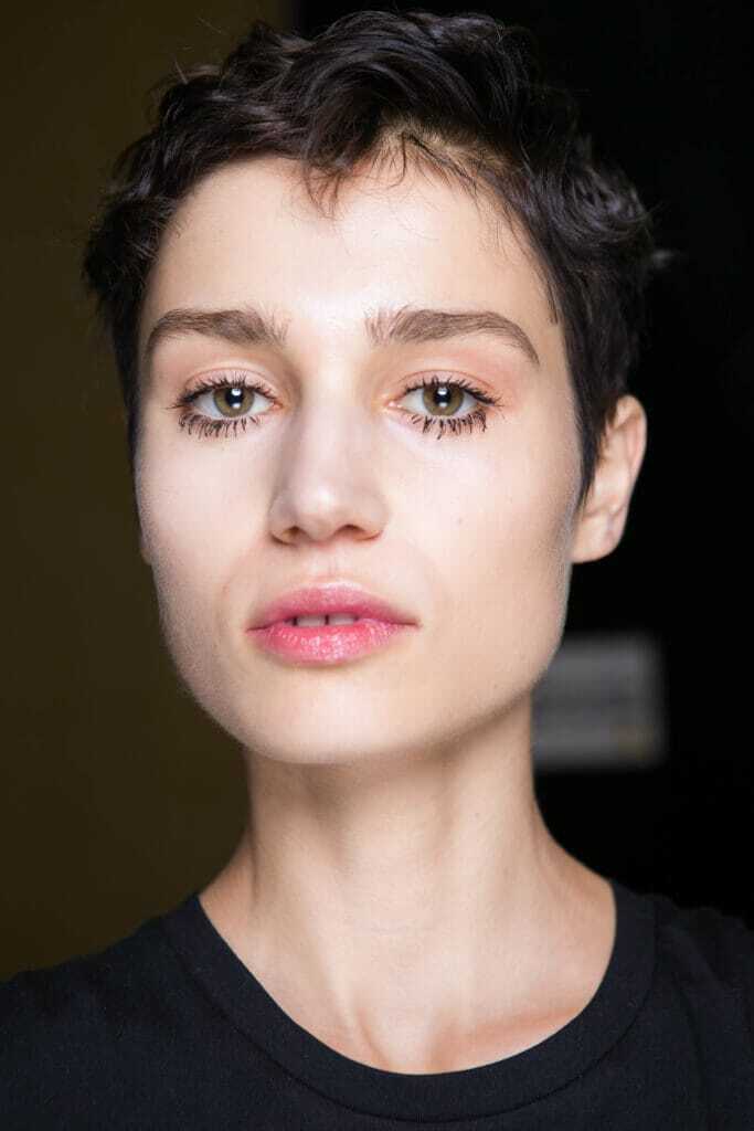 Short hairstyles for thick hair: Model backstage at fashion show with dark brown pixie cut. Model is fresh faced with minimal makeup.