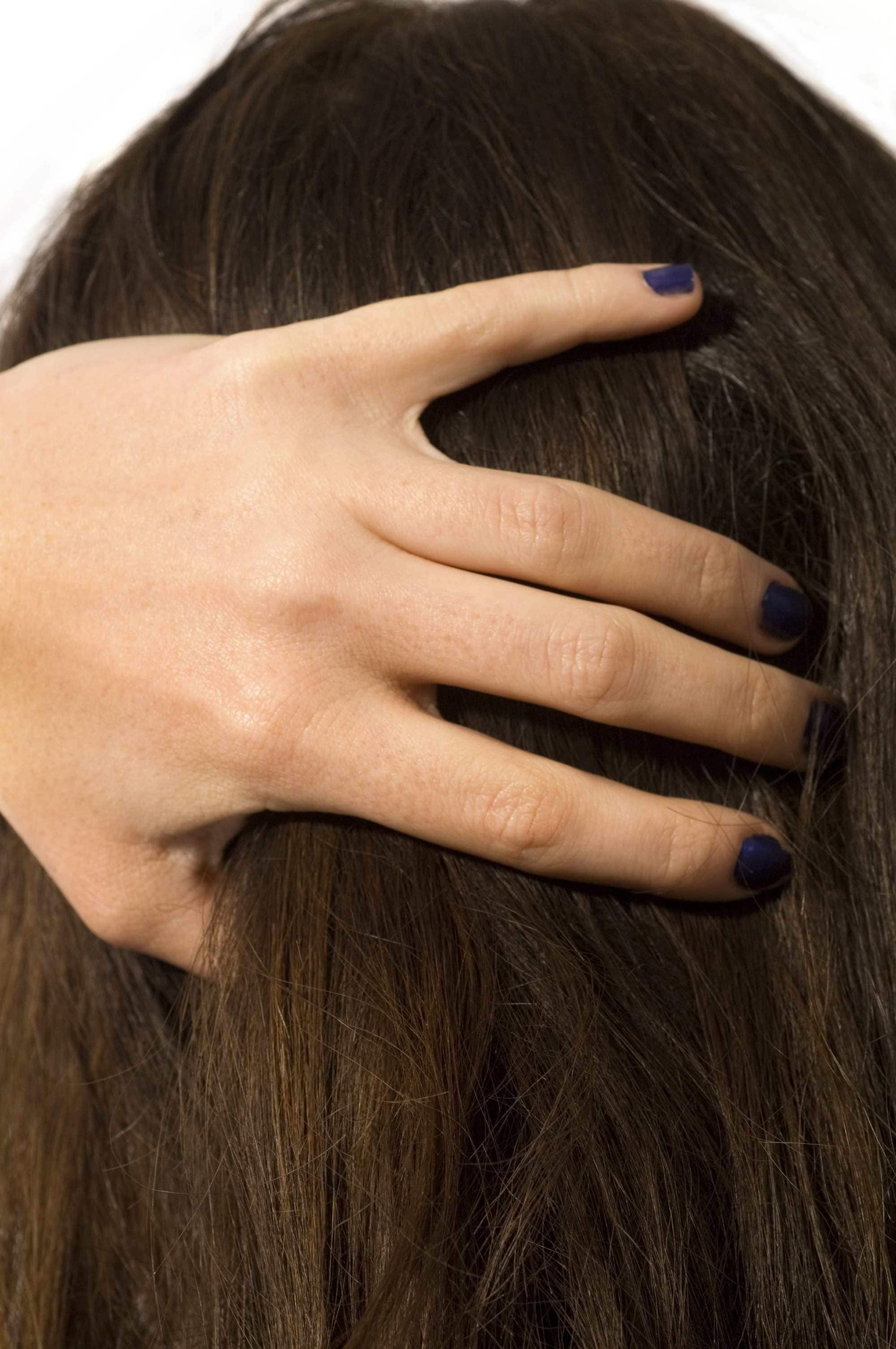 Itchy scalp: Close up image of a woman running her fingers through straight brown hair.