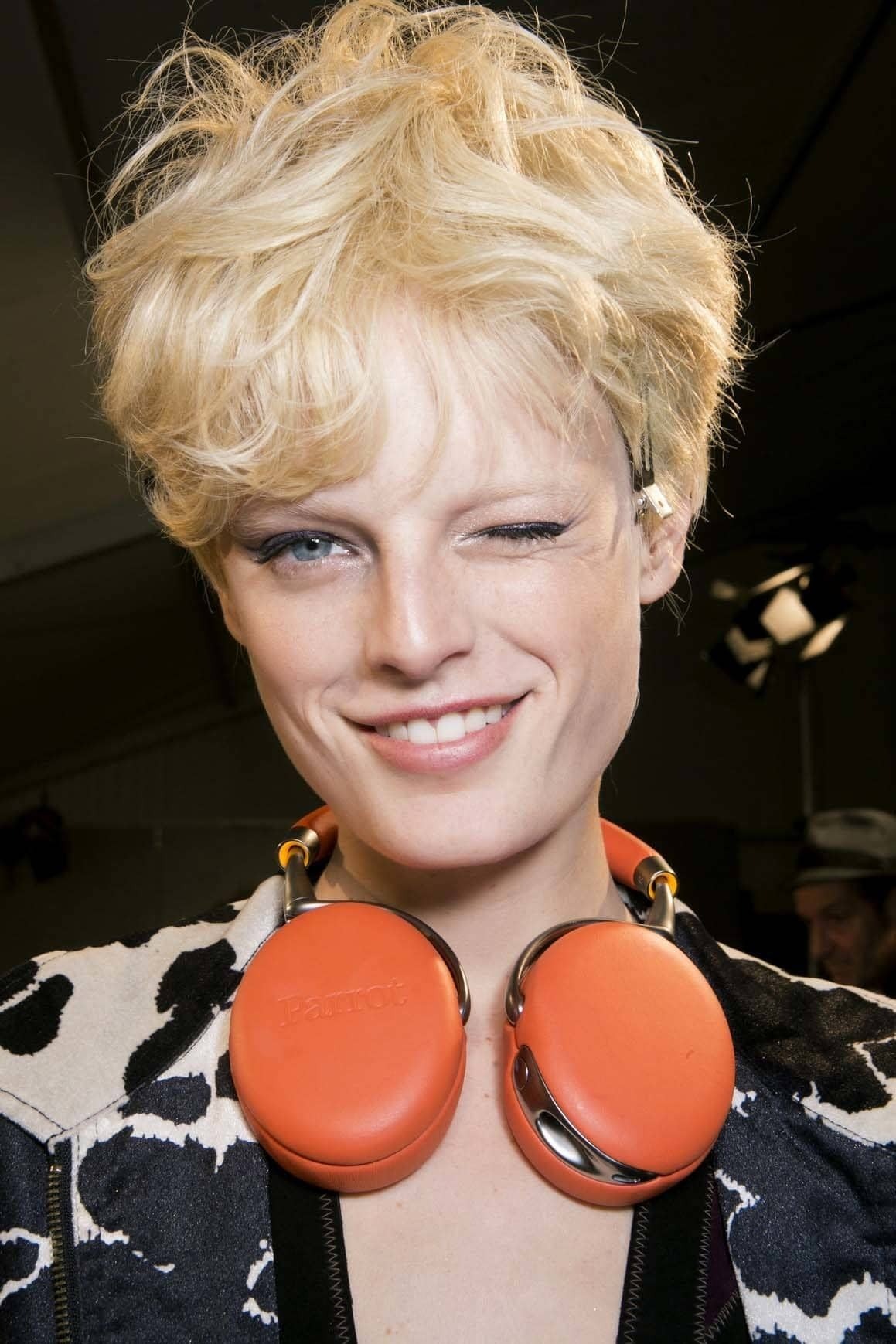 Short hairstyles: Woman with tousled blonde pixie cut wearing orange headphones around her neck.