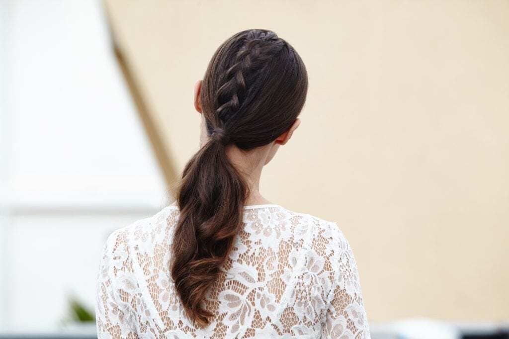 Woman with brown hair in low ponytail with unicorn braid down the middle.