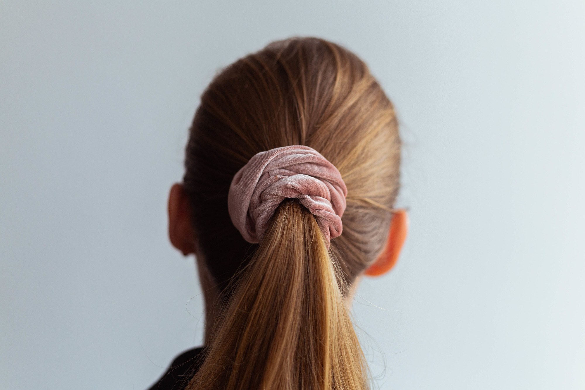 back-shot of a girl with straight, light brown hair tied up into a ponytail with a pastel pink scrunchie