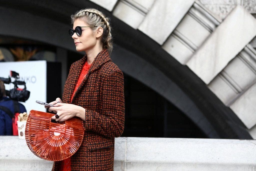 Woman with straight blonde hair in Dutch braids bun wearing sunglasses and holding a basket bag.