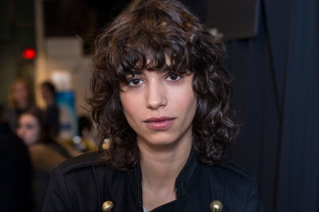 Curly hair: Woman with curly brown shag haircut with bangs wearing a black jacket.