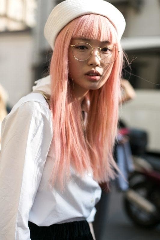 Street style image of woman with pastel pink straight full fringe. Woman is wearing a grey stone coloured beret, metal rim circle glasses and a white top.