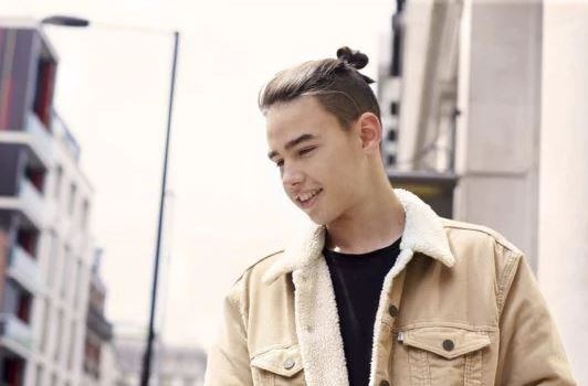 Man bun: Male with brown straight hair in shaved undercut man bun style wearing a cream borg jacket.