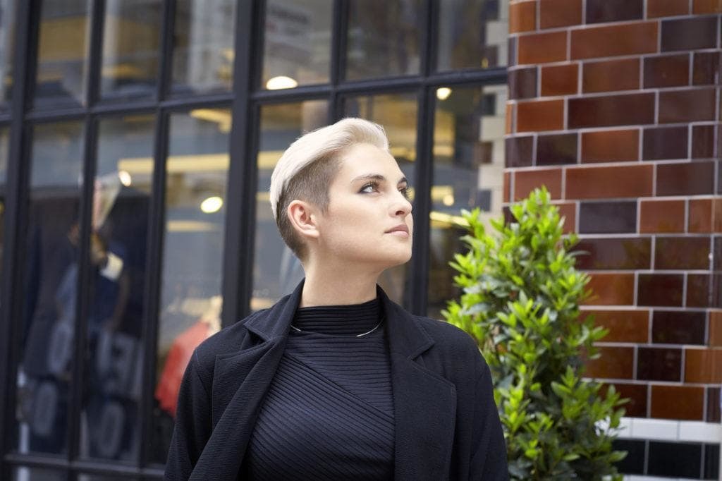 Short hairstyles: Woman with platinum blonde short hair with undercut finish. Woman is wearing all black in this outside image.