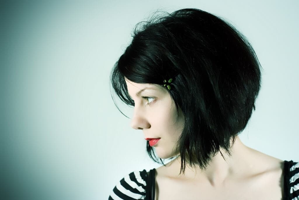 Short hairstyles for thick hair: Side view of a woman with a stacked dark brown hair with a soft fringe. Woman is wearing a striped top and red lipstick.