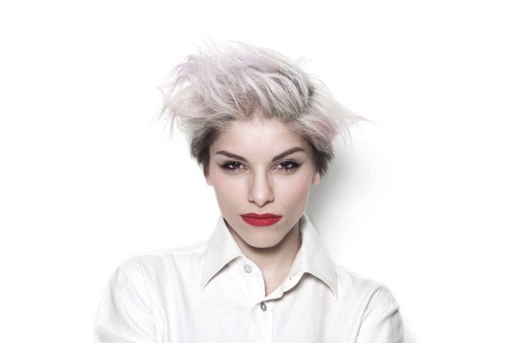 Short hairstyles: Woman with short bleach blonde straight hair styled spiky. Woman is wearing a white shirt and bold red lipstick.