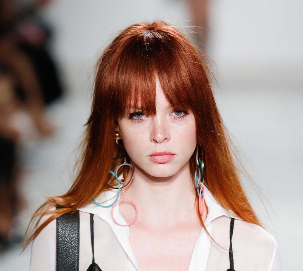 Red hair: Model on runway with fiery auburn straight hair with long fringe bangs wearing a white blouse.
