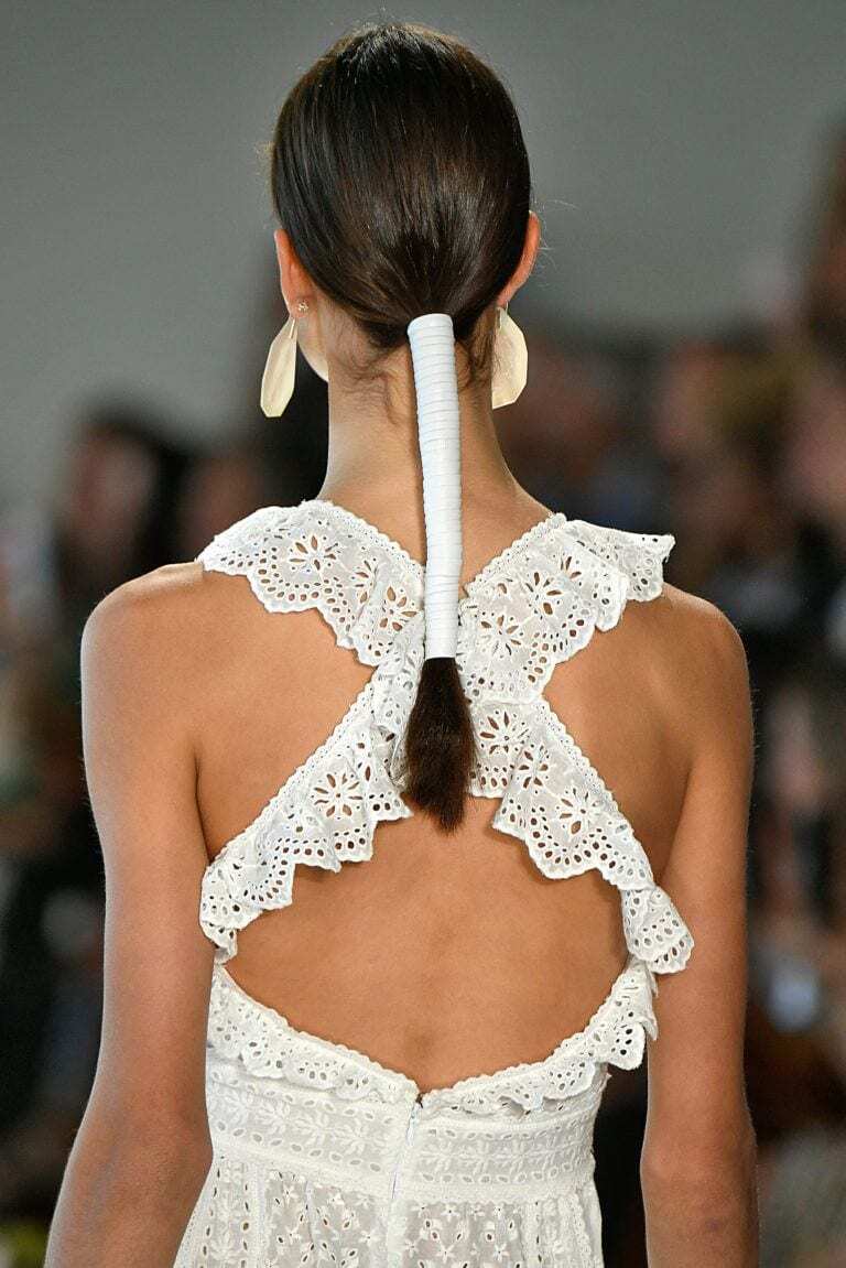 Back view of woman with a low ponytail with a white leather wrap. Woman is wearing a white broderie summer dress.