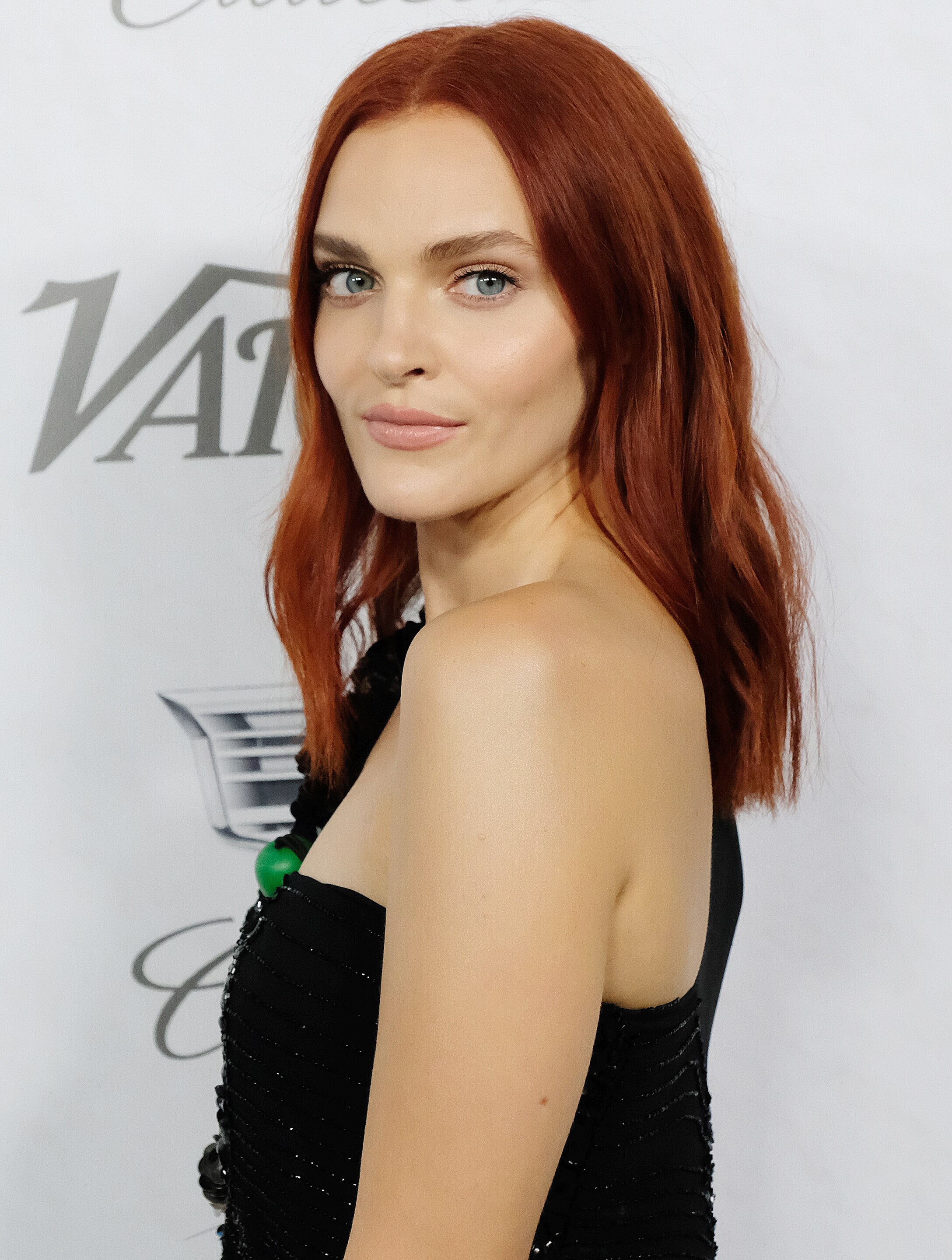 Madeline Brewer medium length deep copper hair colour wearing a black off the shoulder dress with natural makeup.