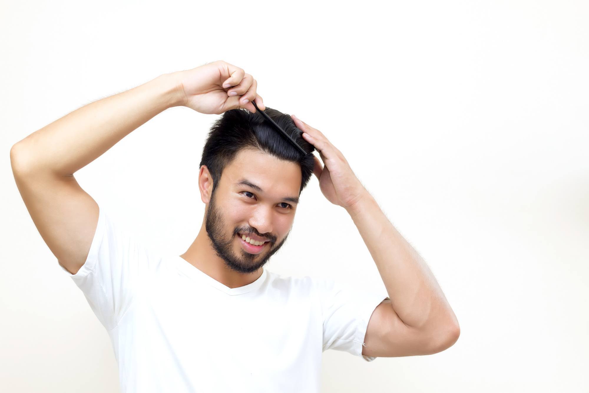 hair growth for men: smiling man brushing hair with comb on white background