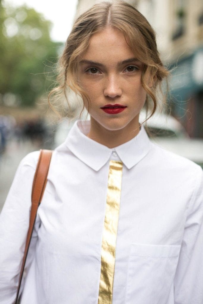 Fringe hair: Woman with curly blonde hair in updo with soft bangs. Woman is wearing a white shirt and red lipstick.
