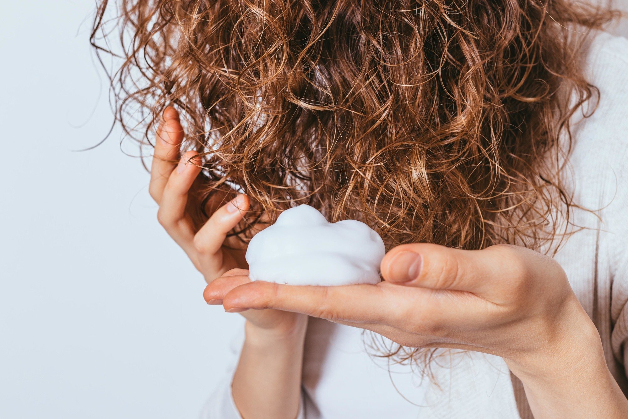 adding volume: woman applying hair mousse to wavy copper hair