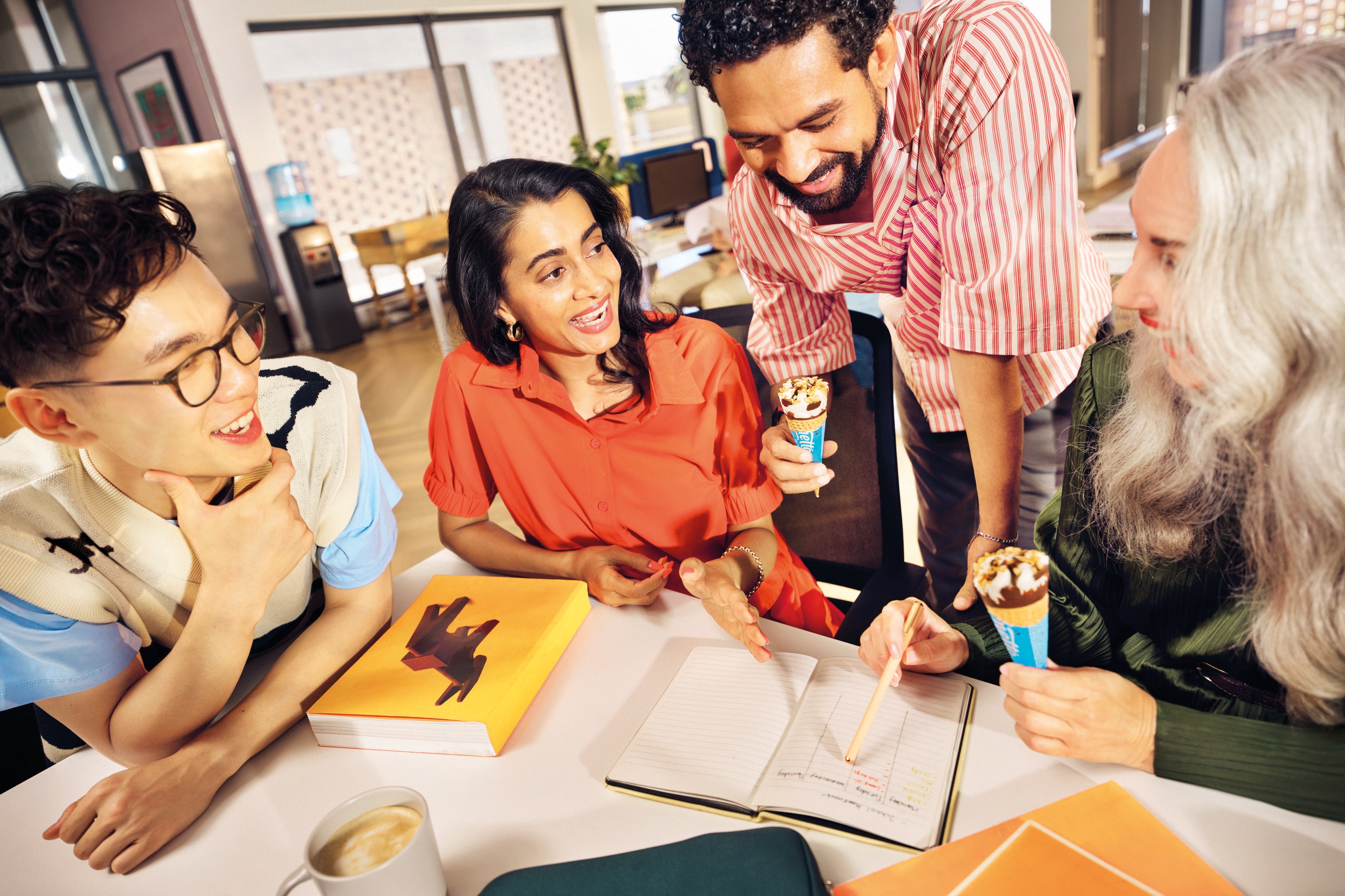Group of colleagues sharing Cornetto ice cream treats while gathered around a table with notebooks.