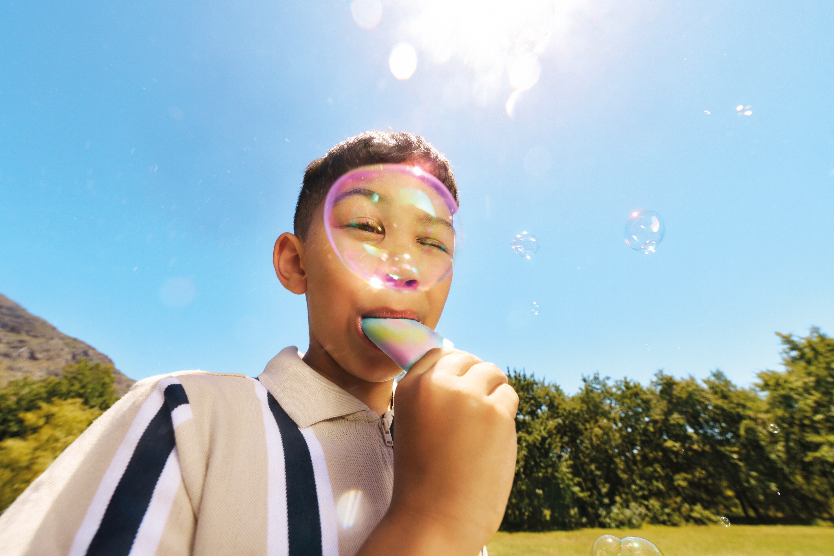 Boy eating ice lolly outside with bubbles floatin