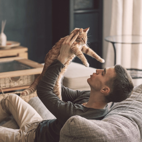 Young man playing with a cat on his couch with no sign of allergies or sensitive skin