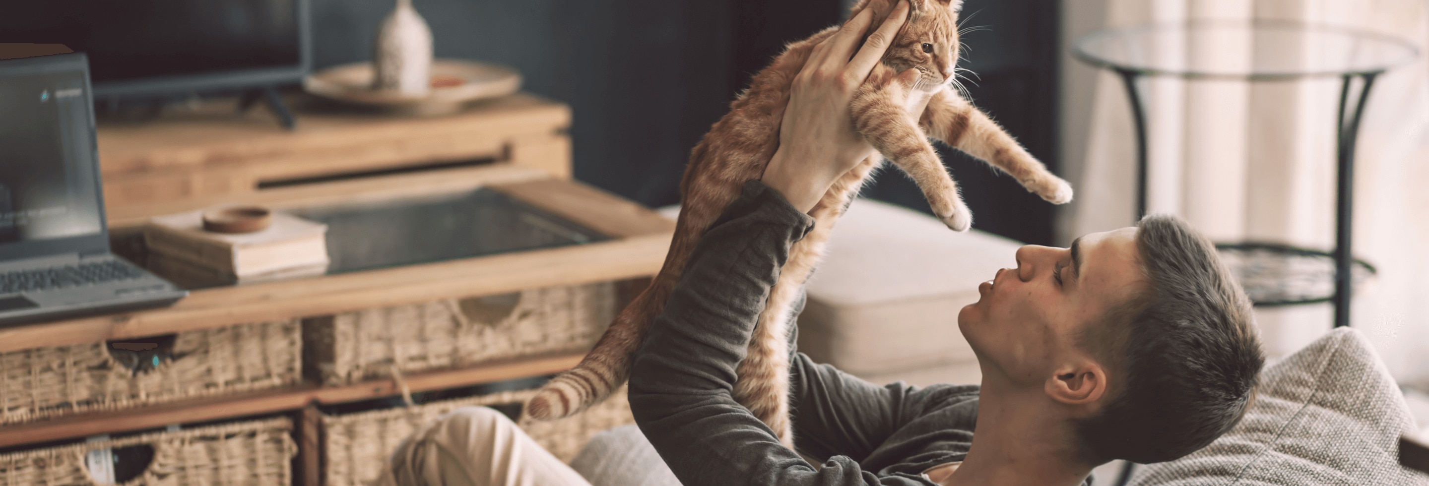 Young man playing with a cat on his couch with no sign of allergies or sensitive skin 