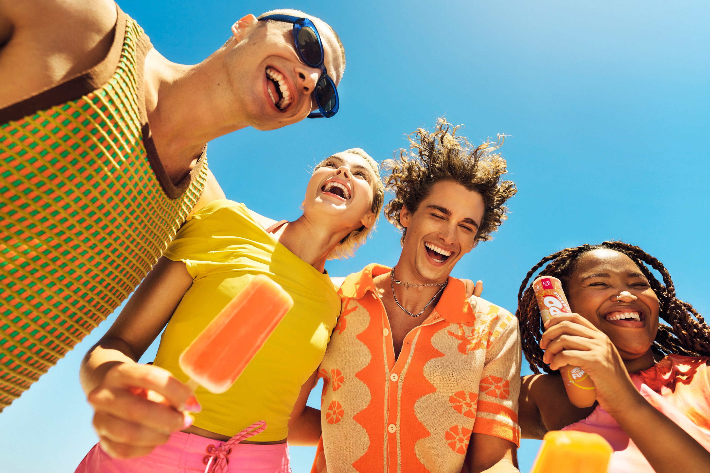 Group of people laughing and holding an ice lolly against a blue sky