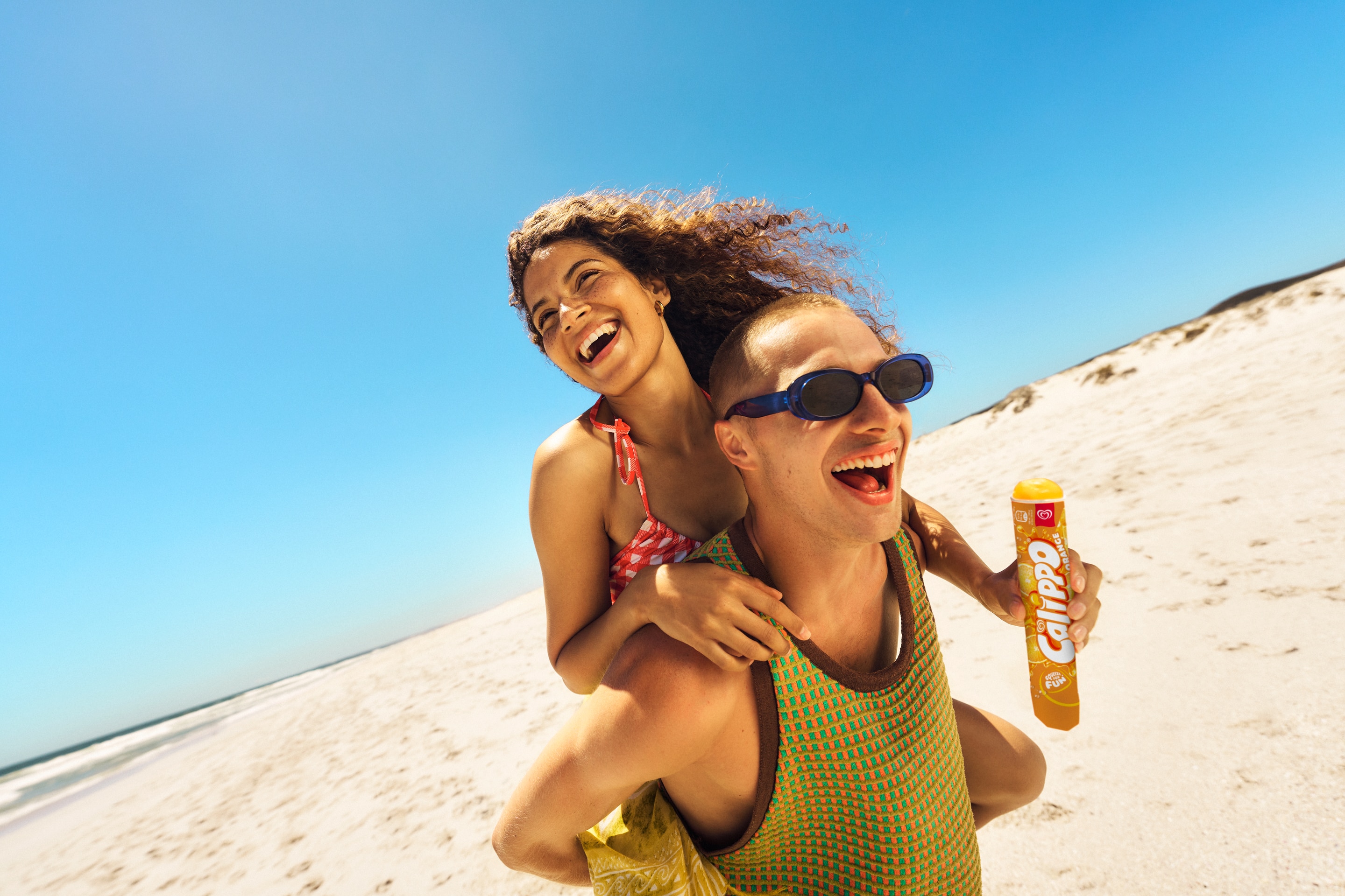 Couple smiling on the beach with an ice lolly against a blue sky