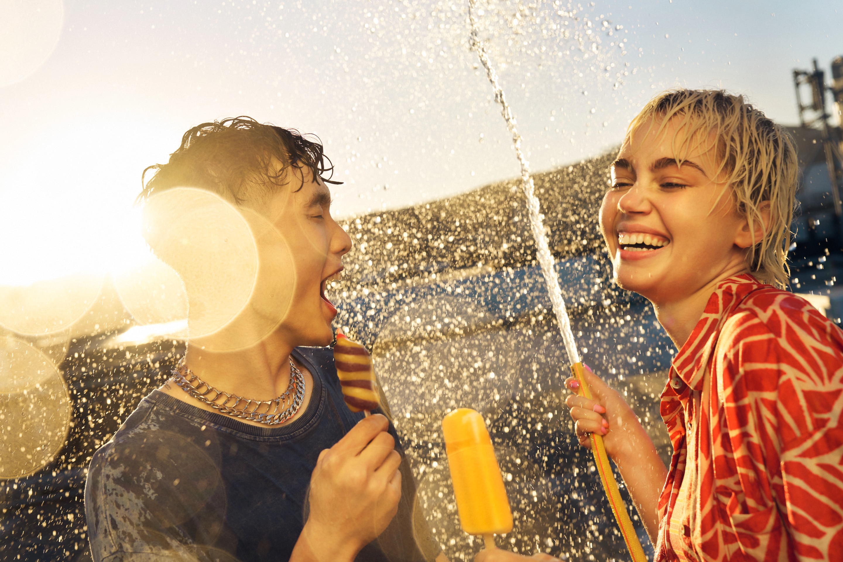 Couple holding an ice lolly and a hose shooting water