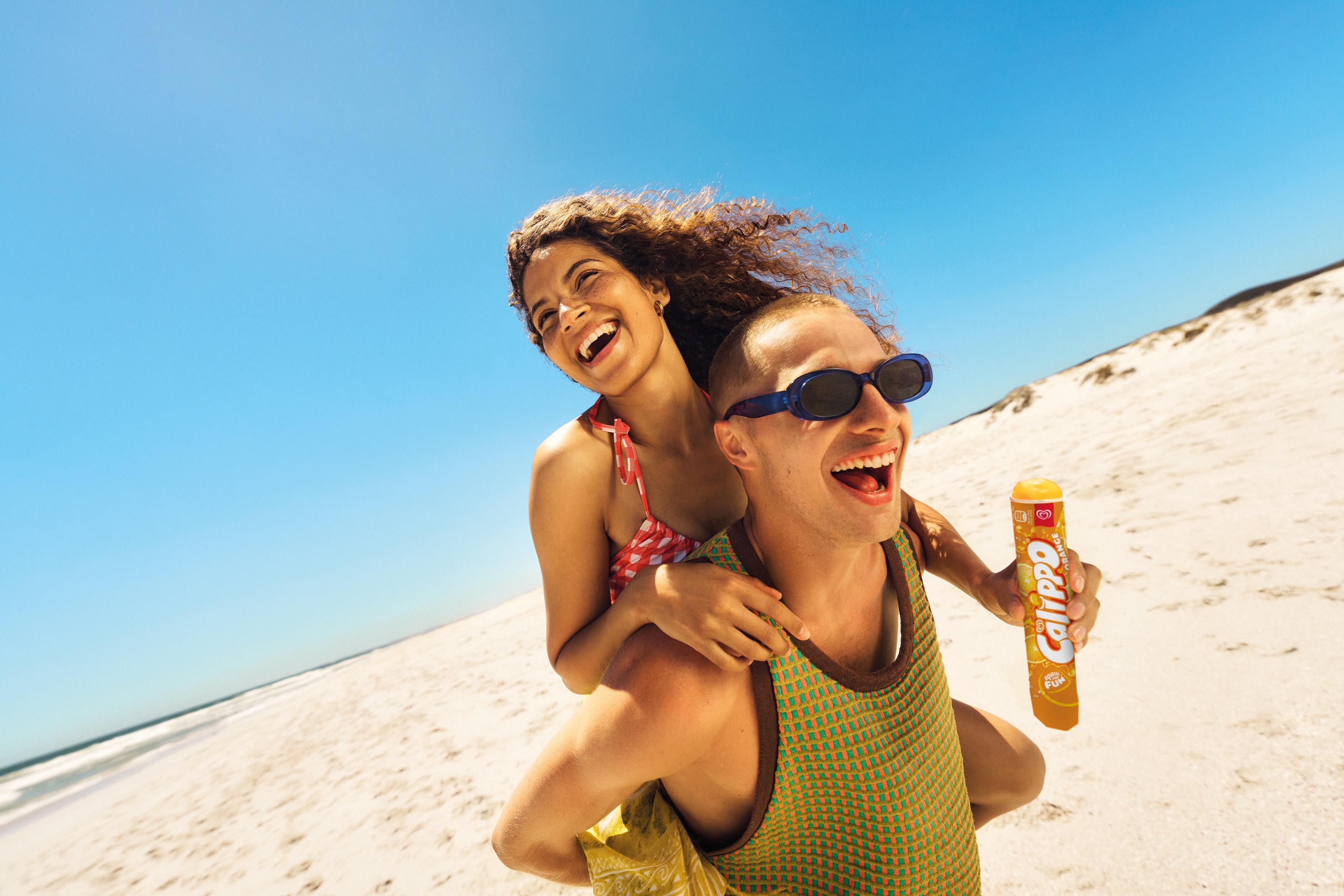 People enjoying a Calippo ice lolly on the beach against bright blue sky.