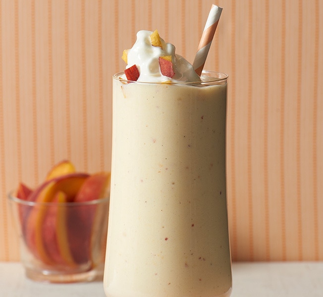 Glass of peaches milkshake with peach slices in the background