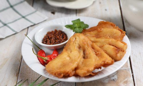 Pisang goreng sambal roa disajikan di atas piring yang diletakkan di atas meja kayu aneka gorengan.