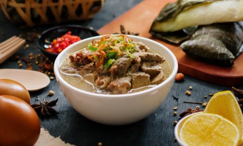 Semangkuk menu Lebaran khas Sulsel, coto makassar dengan lontong di belakangnya.