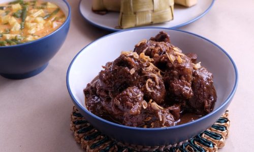 Satu mangkuk bumbu semur daging di belakangnya ada ketupat dan sayur nangka.