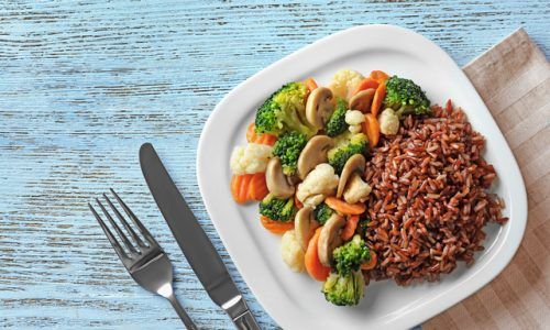 Sepiring menu sahur sehat berupa nasi merah dan sayuran dengan garpu dan pisau di sampingnya