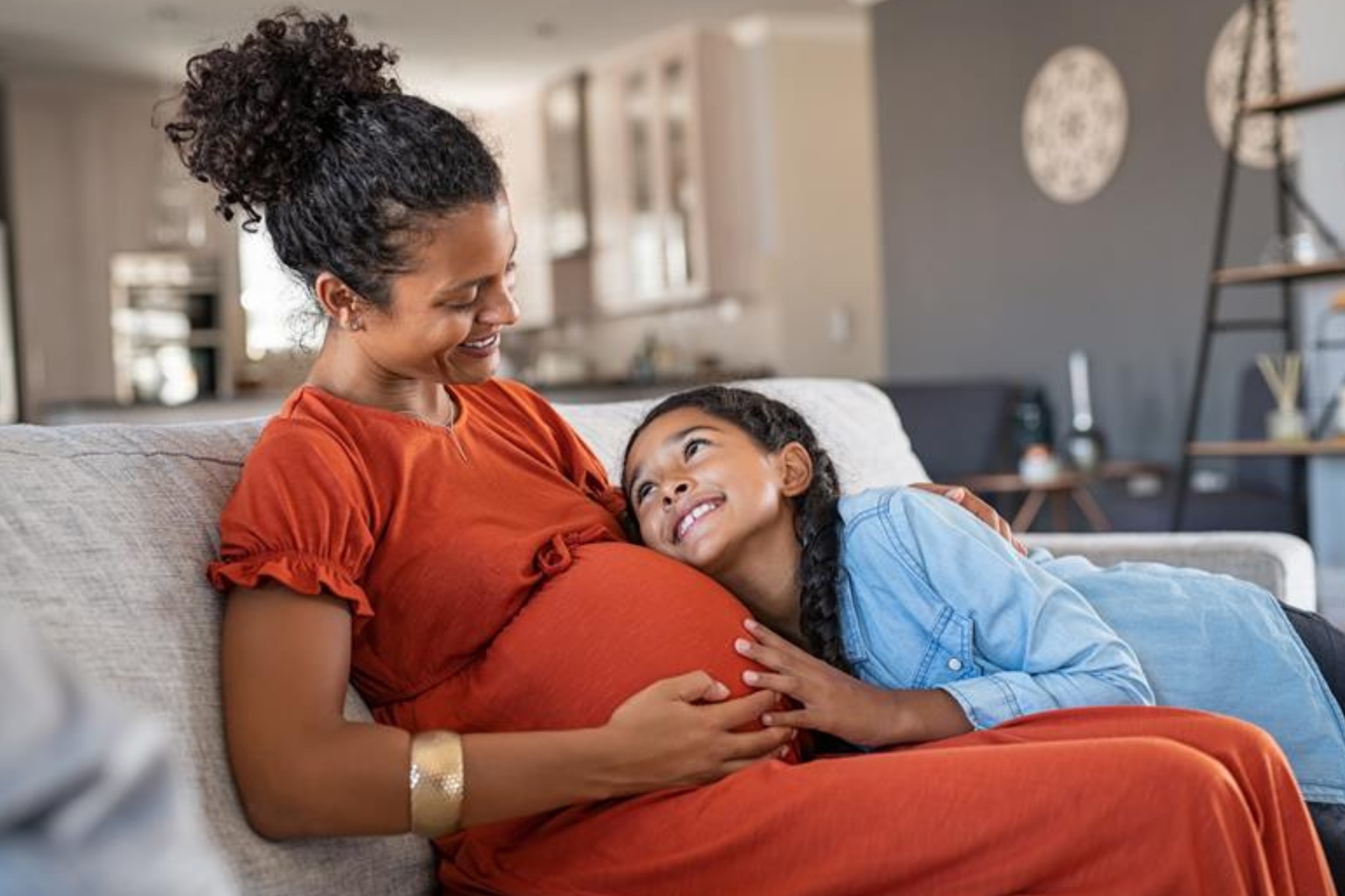 Mother and daughter sitting together in living room while Mom is pregnant