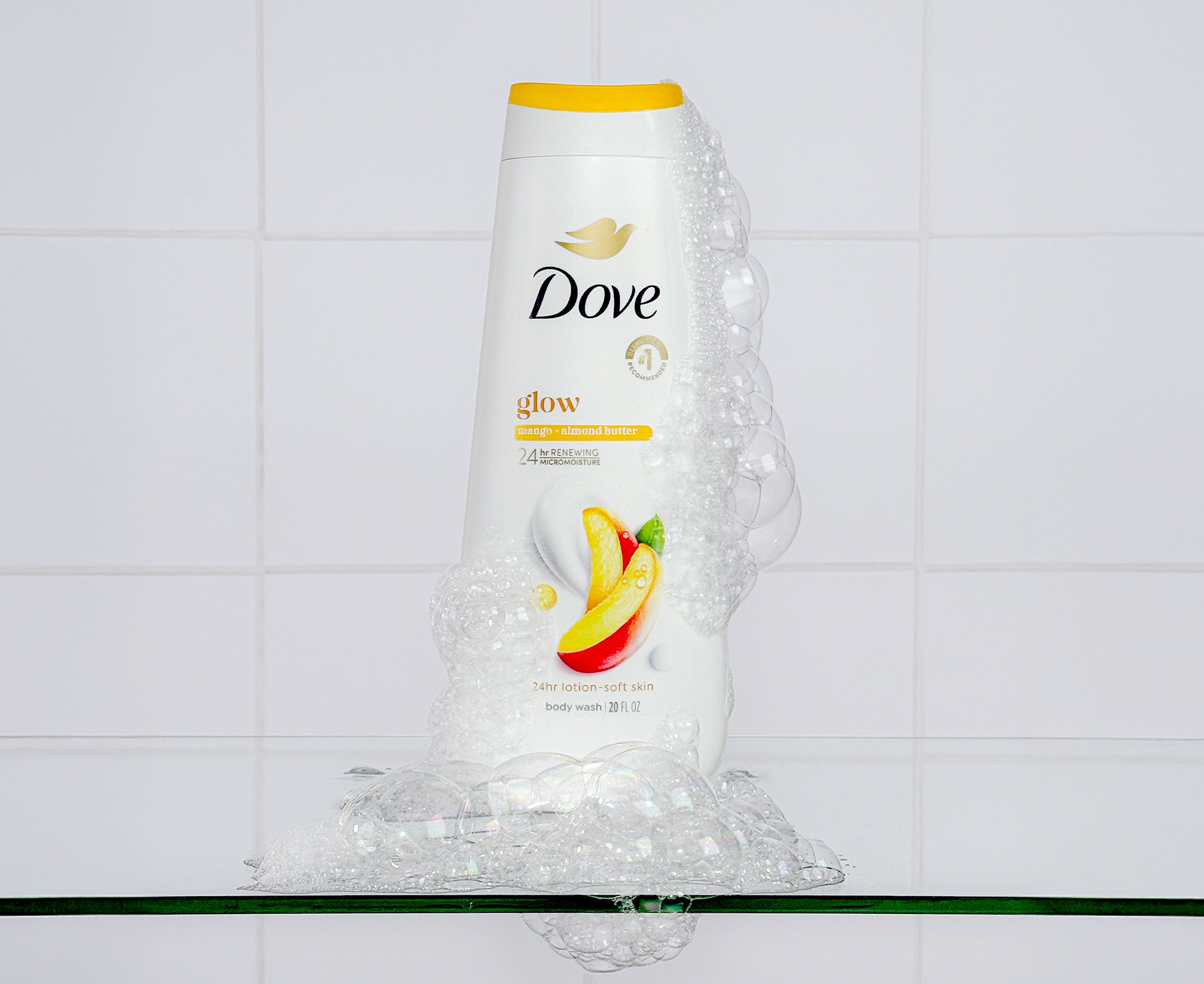 Dove Glow Body Wash standing on a glass shelf with foamy texture across the side and at the bottom of the bottle 
