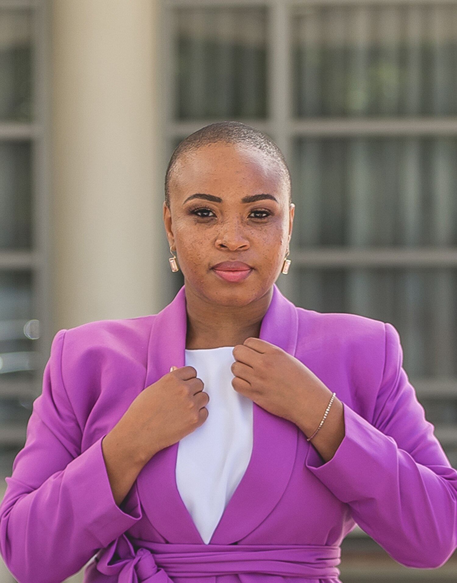 Hulisani Ravele standing infront of an office building wearing a purple blazer 