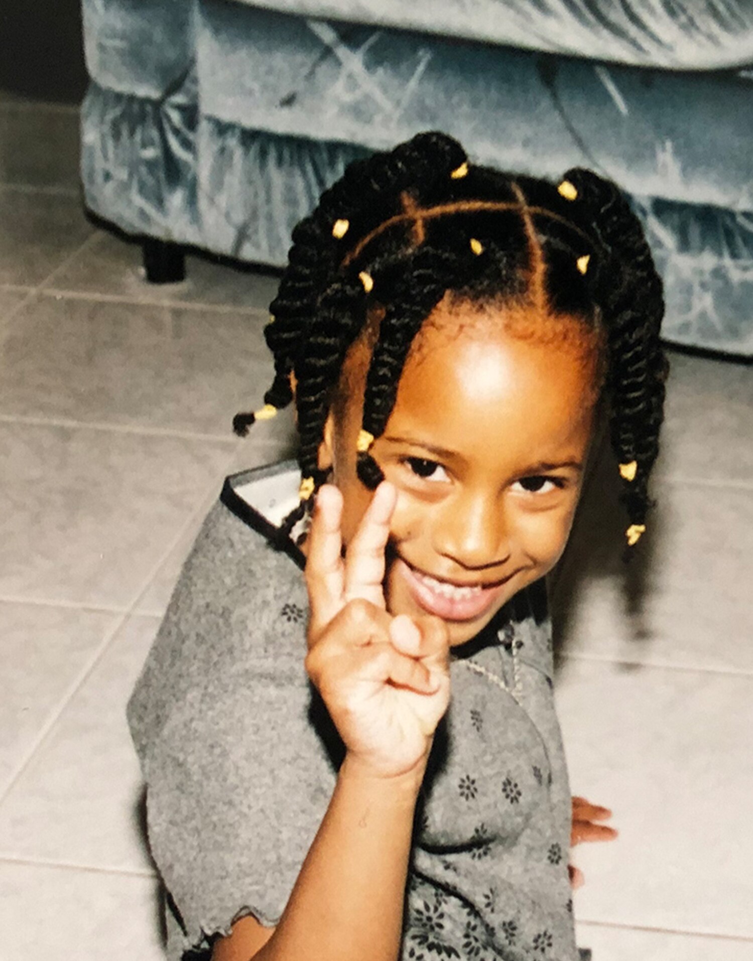 Asha Bromfield as a child sitting on a tiled floor smiling 