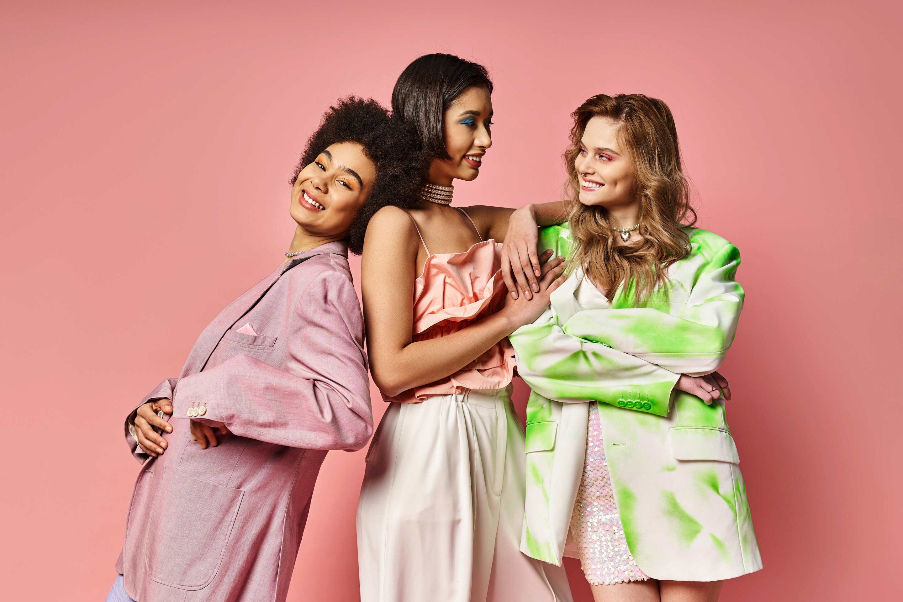 สาวผิวสองสี ยืนกลาง แต่งตัวโทนสีชมพูโอลด์โรส ขนาบข้างด้วยสาวผิวสีแทนเข้มน้ำตาล เสื้อผ้าโทนชมพู และสาวผิวขาวเสื้อลายเขียวขาว