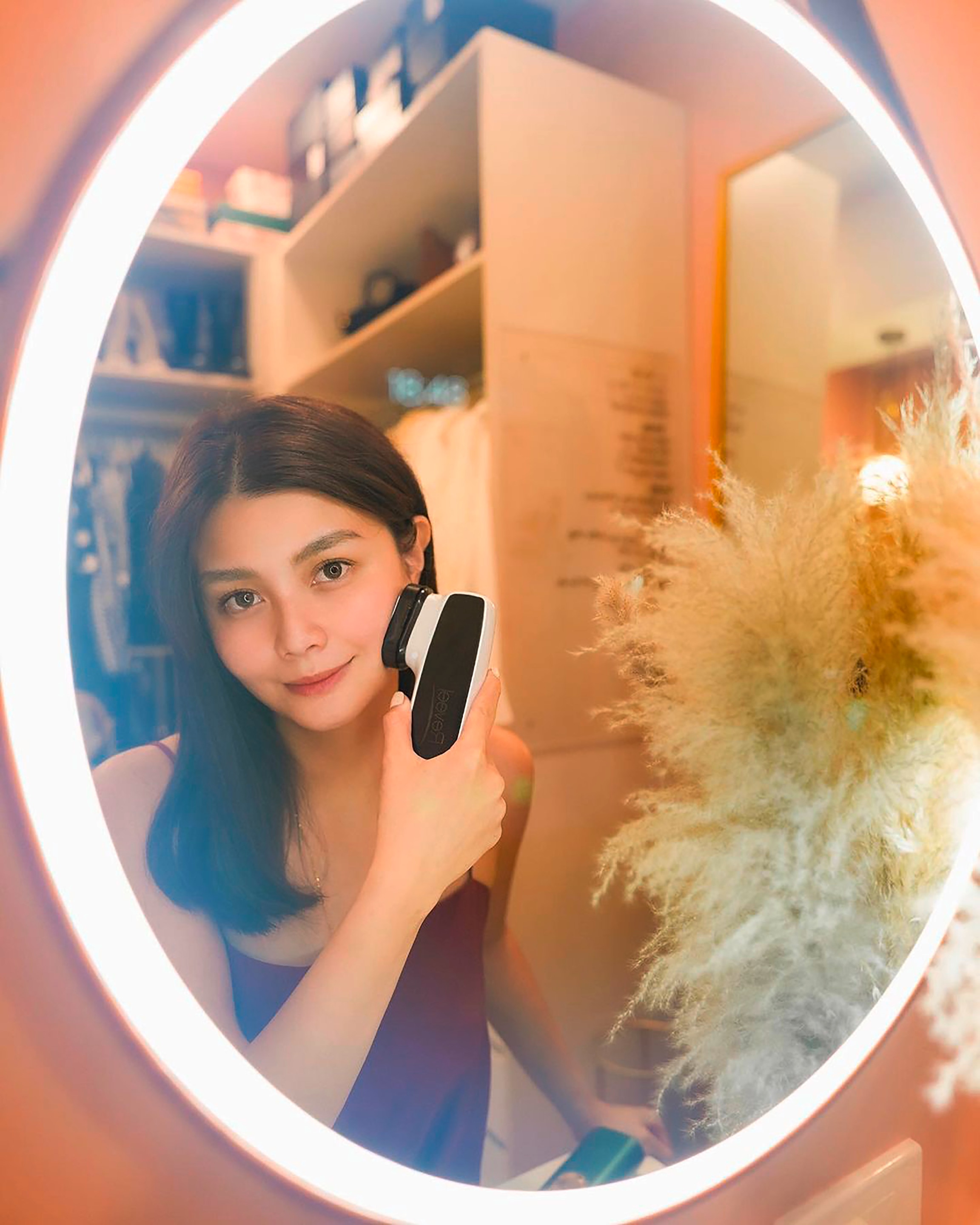 Woman using radio frequency wand in front of a mirror.