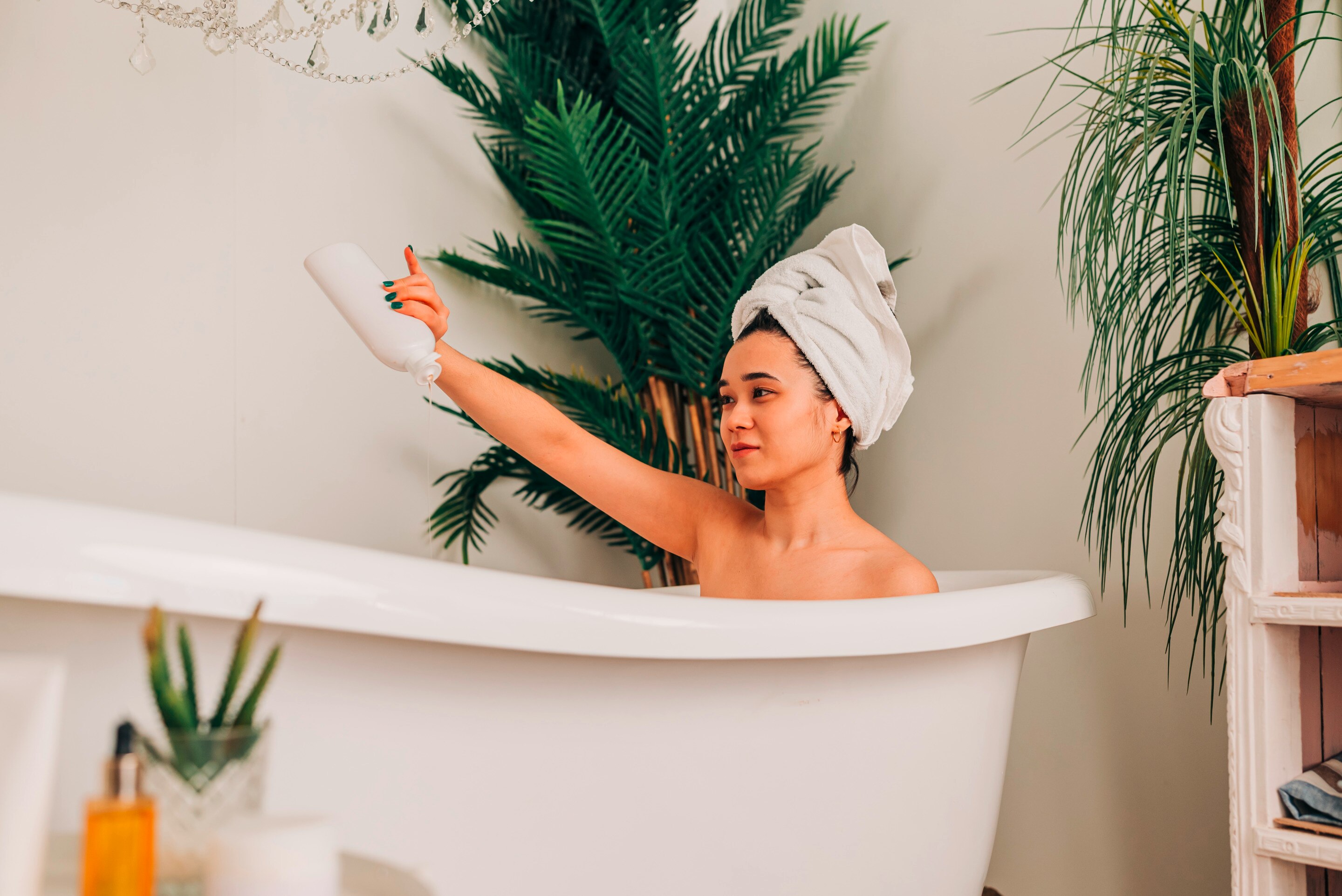 Woman with her head wrapped in a towel pouring body wash into her bath.