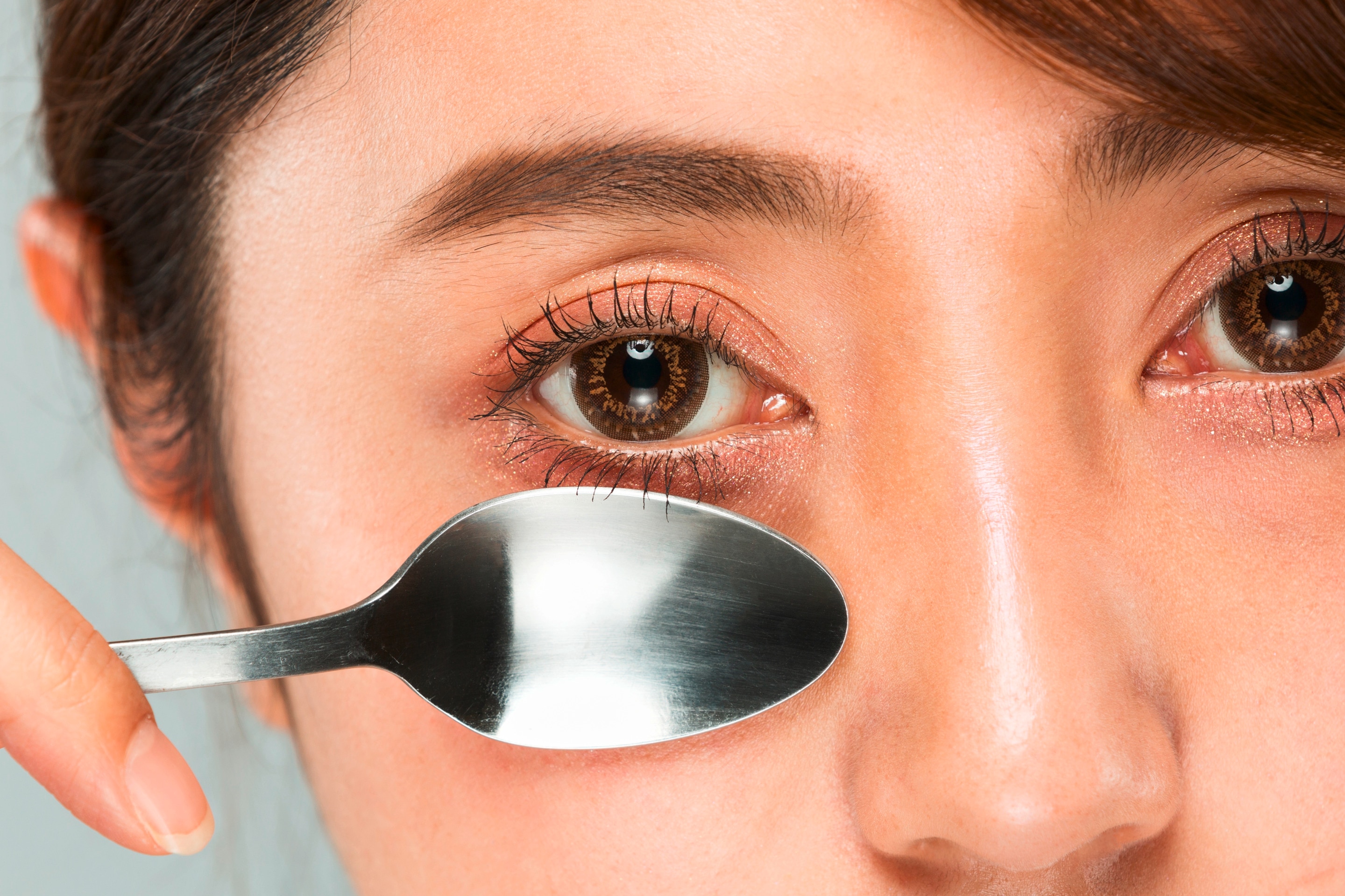 Woman massaging her under-eye area with cold spoon.