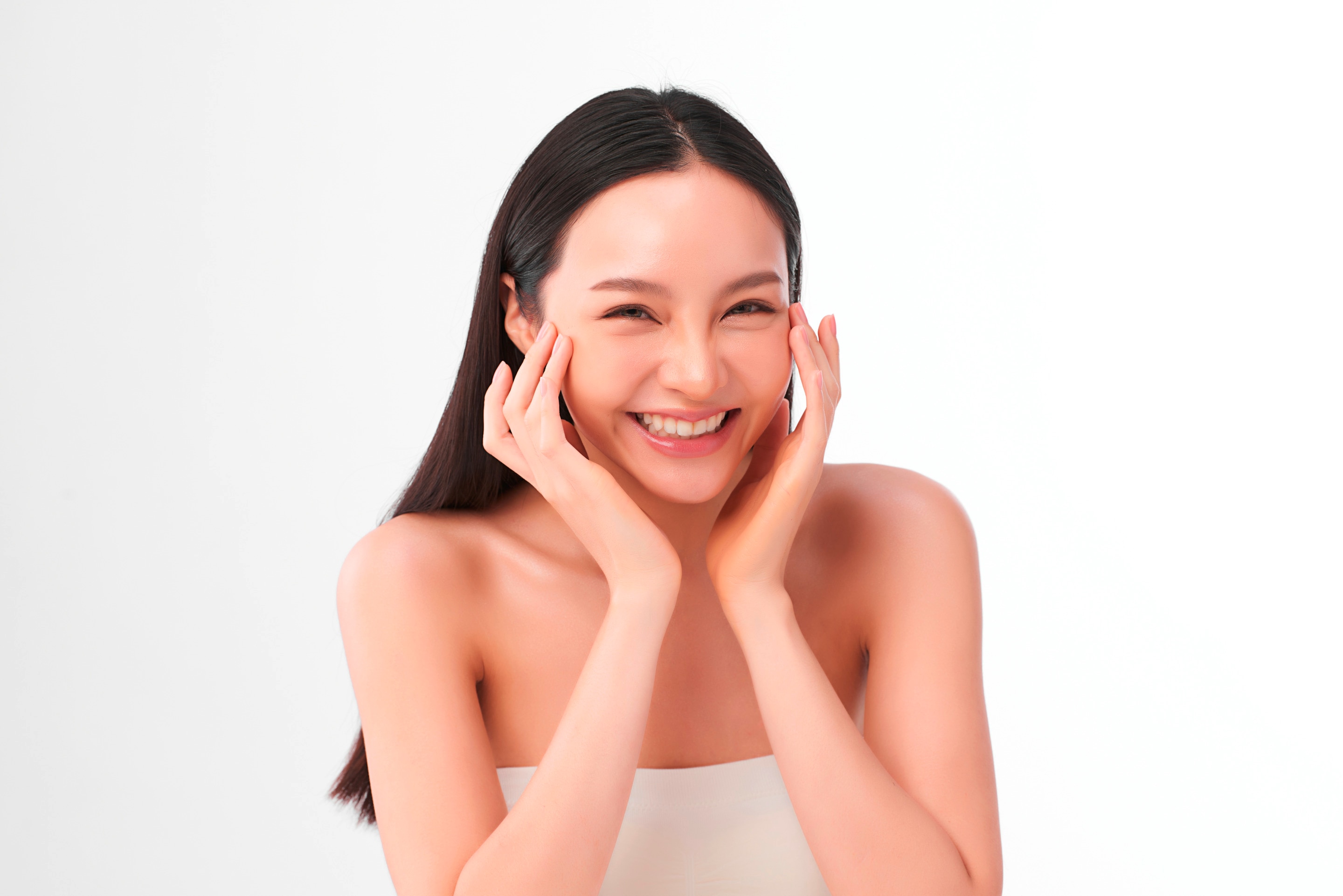 ผู้หญิงเอเชีย ผมตรง ผมยาว แสกกลาง ยิ้มเห็นฟัน นิ้วกดแตะหน้า นิ้วแตะโหนกแก้ม สวมเกาะอกสีขาว 