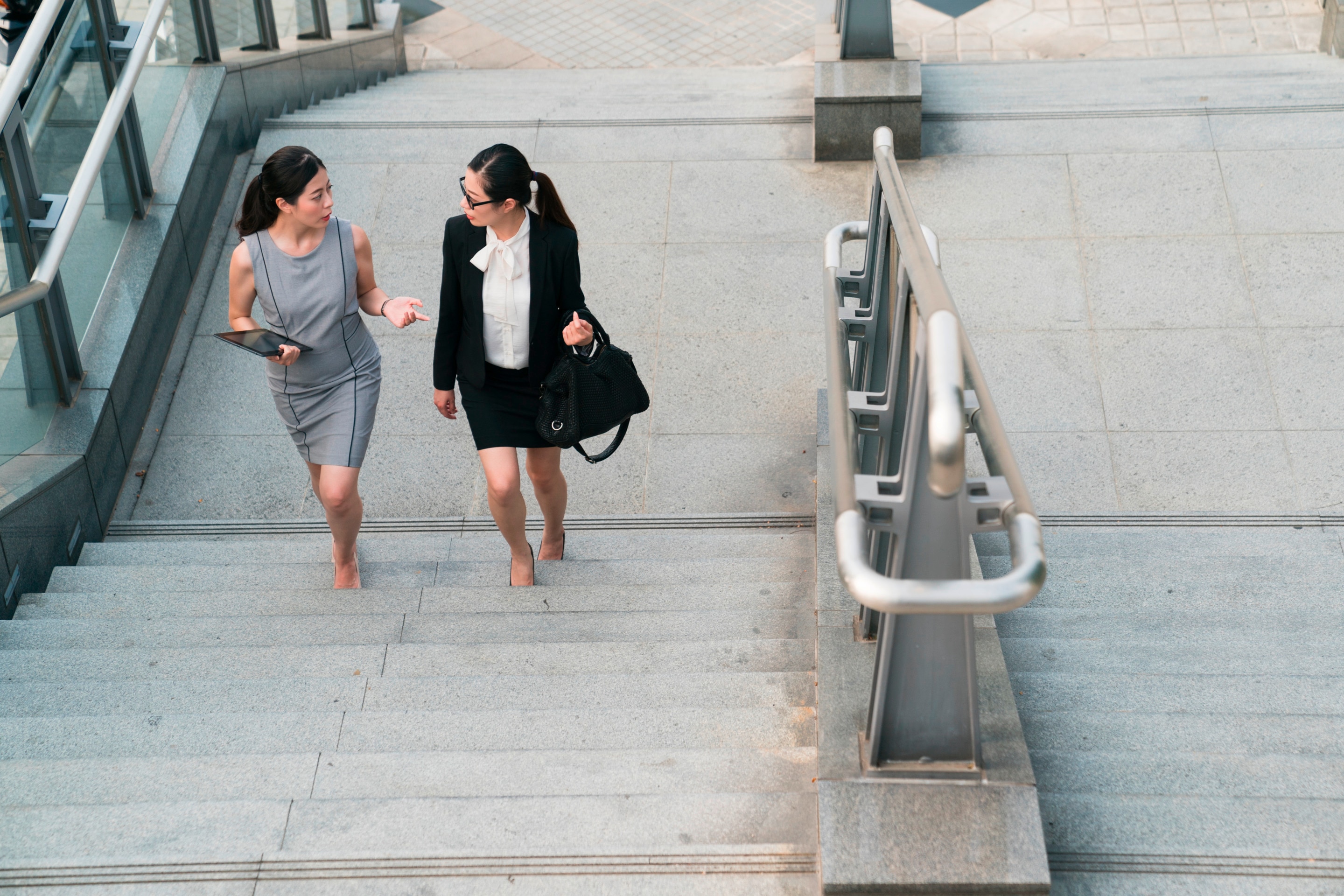 Two women in smart casual clothing climbing up stairs.
