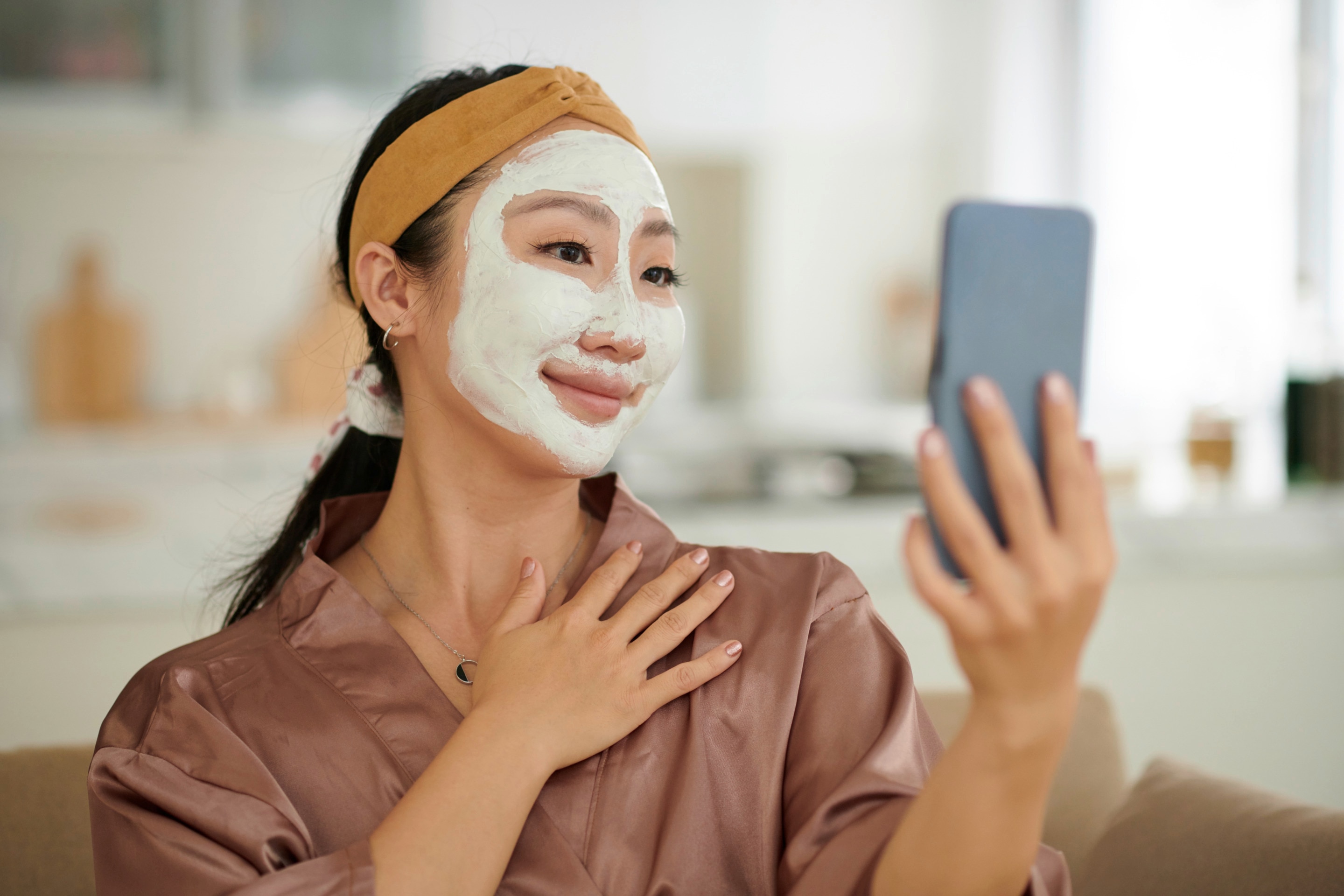 Woman with clay mask on her face taking a selfie with her phone.